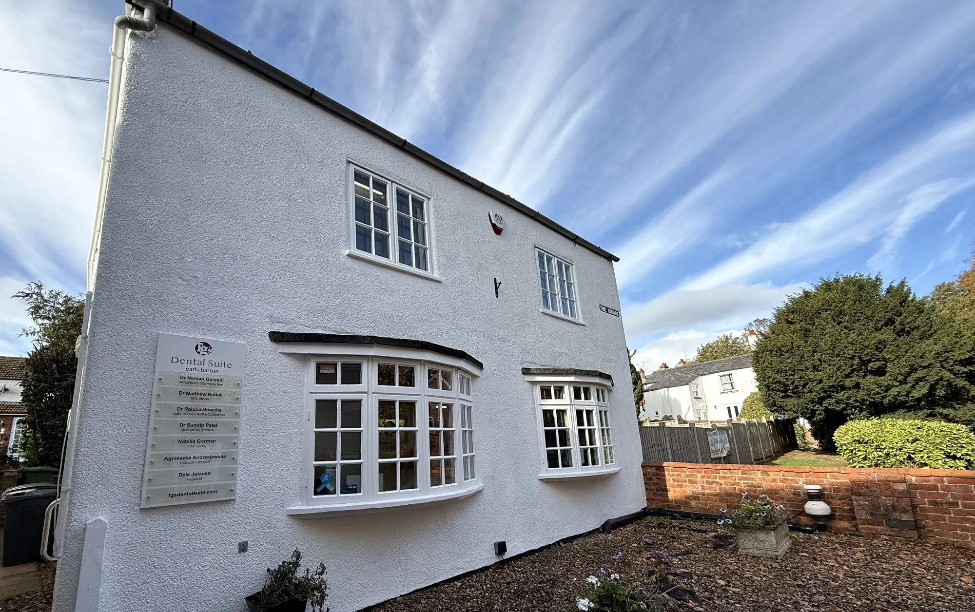 The white rendered TG's Dental Suite Earls Barton building, with the clinician name-board beside the bay window