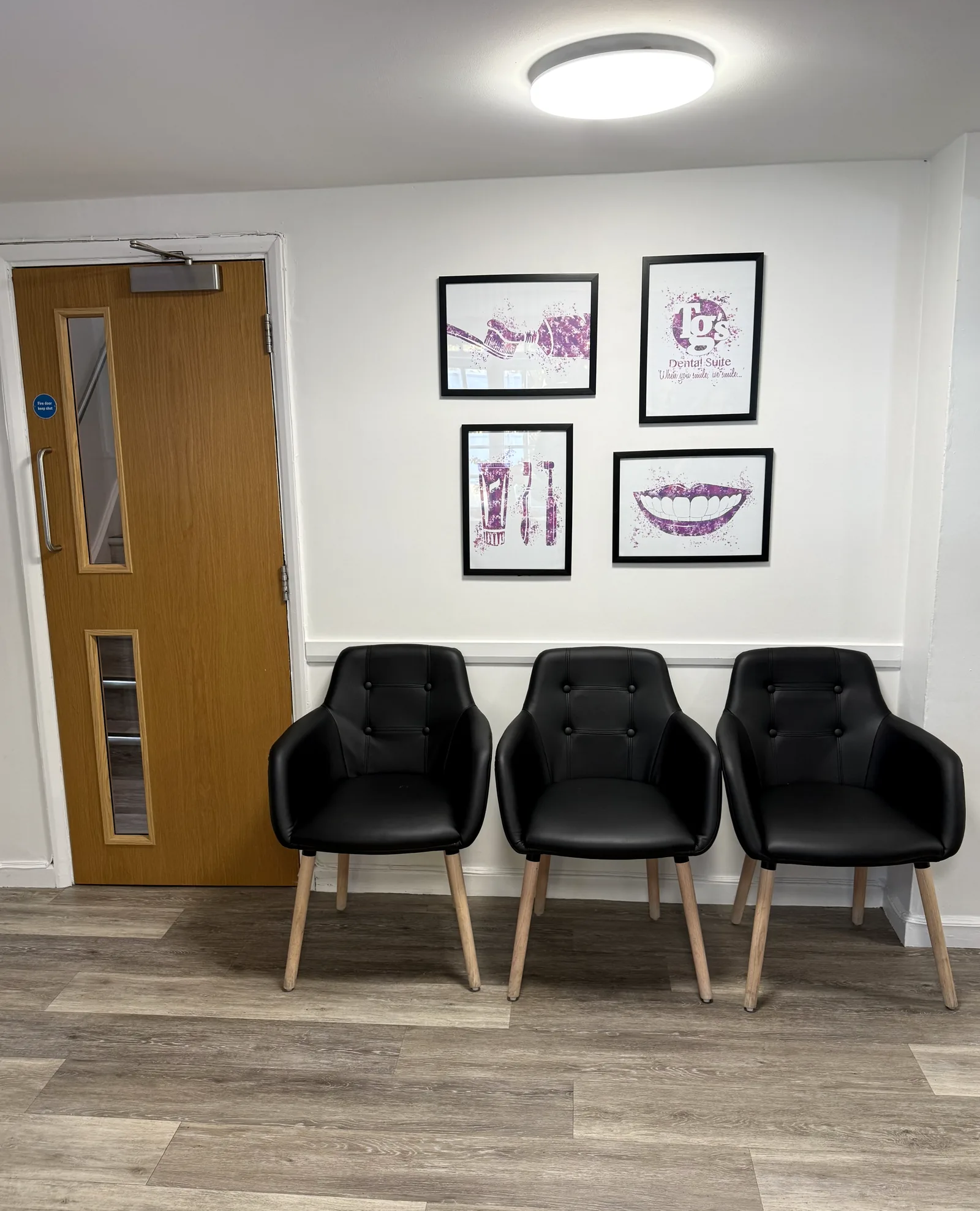 Three black waiting-room chairs under four framed prints, beside the surgery door